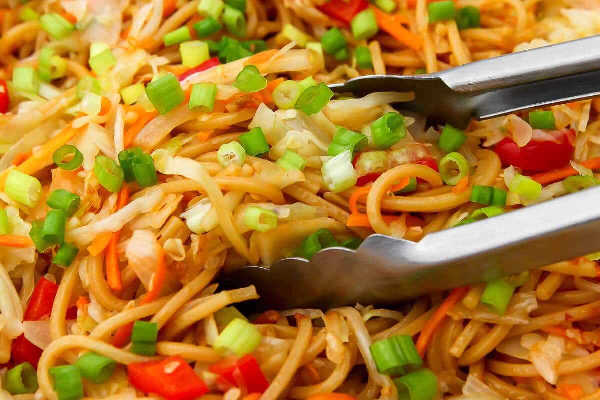 A close of of spicy Hakka noodles being picked up with tongs.