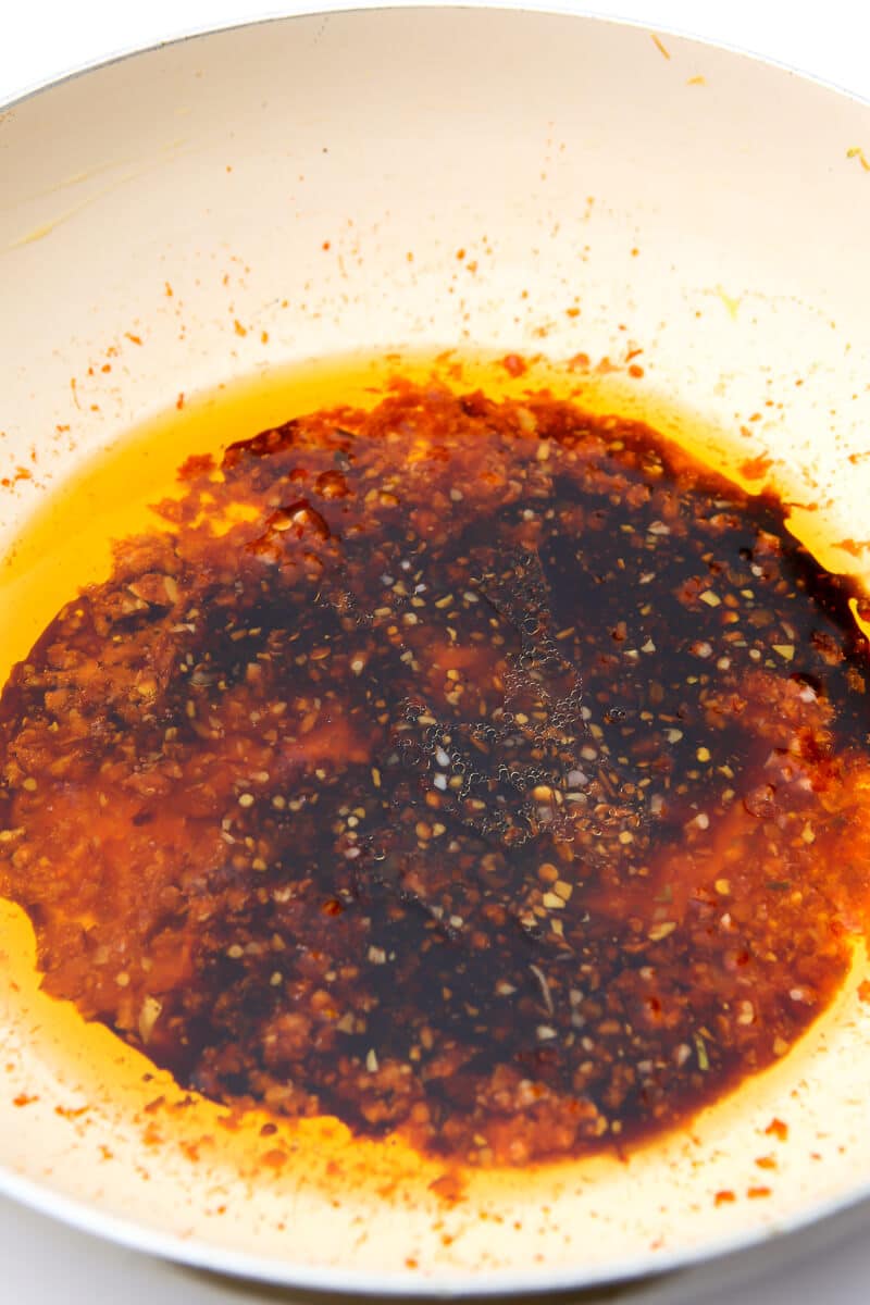 Oil, garlic chile sauce, soy sauce, and rice vinegar in a white wok to make the sauce for Indian Hakka noodles.